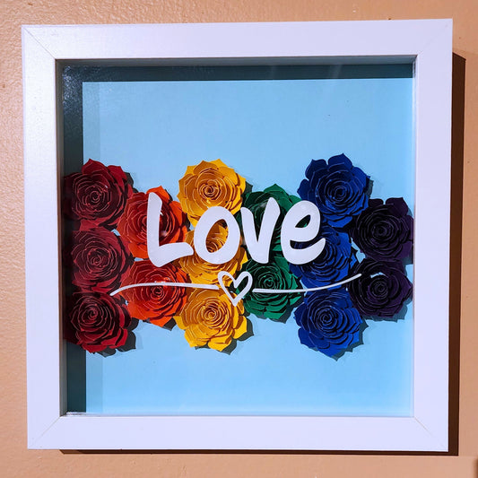 Framed shadowbox artwork with rainbow-colored paper roses with 'LOVE' text white vinyl on a light blue background.